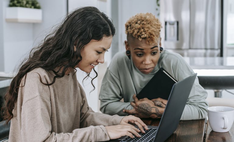 Two women sharing a happy moment while using a laptop indoors. Smiling and engaged.